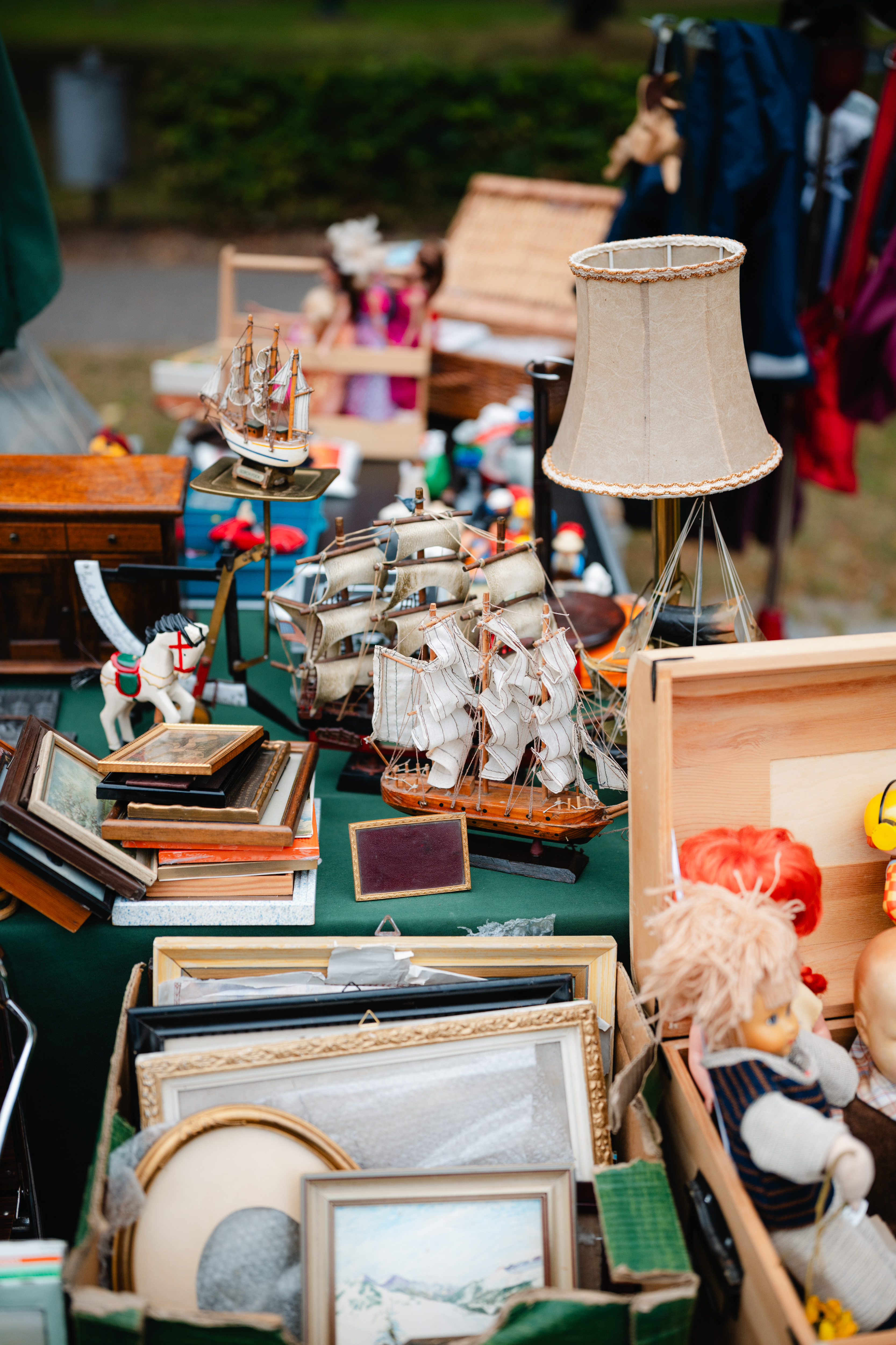 Ein Flohmarktstand zeigt Modellschiffe, Bilderrahmen, eine Lampe und Spielzeug. Verschiedene Vintage-Artikel sind auf einem Tisch ausgestellt.
